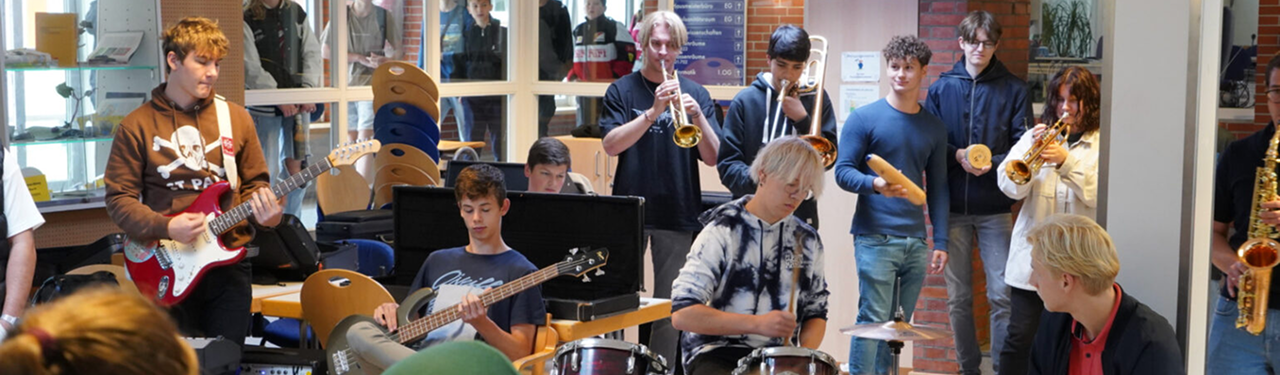Eine Schülerband mit Trompeten, E-Gitarre, E-Bass und Schlagzeug spielt in der Pausenhalle